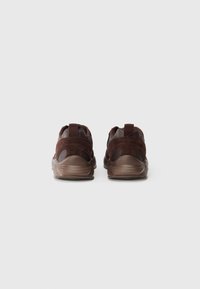 Pair of brown sneakers with suede accents viewed from the back on a plain white background.
