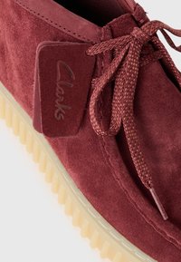 Bordeaux mokkasinsko skinn med matchende vevde snørebånd, gummisåle, og et skinnmerke med preget "Clarks"-logo.