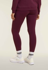 Leggings bordeaux con un design aderente, texture liscia, vita media e abbinati a scarpe sportive bianche e calzini alti.