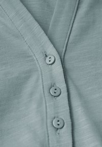 Primo piano di un morbido tessuto di un cardigan blu chiaro con tre bottoni cuciti lungo l'apertura a V.