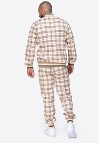 Beige Karo-Trainingsanzug mit passender Jacke und Hose. Verfügt über gerippte Bündchen und Saum, Kontraststreifen und eine strukturierte Oberfläche.