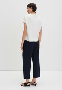 Haut structuré blanc à manches courtes, associé à un pantalon large bleu marine foncé et des sandales à talons noires. Tissu lisse, design minimaliste.