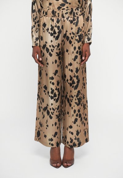 Pantalones de satén de pierna ancha en beige con manchas de leopardo negras, con una cinturilla elástica y textura suave. Combinados con tacones abiertos.