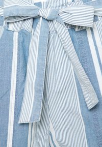 Hellblauer und weiß gestreifter Stoff mit einer gebundenen Schleife an der Taille. Enthält eine Mischung aus einfarbigen und gemusterten Bereichen mit sichtbaren Nähten.