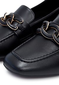 Mocassins en cuir noir avec bouts carrés et chaînes à maillons dorés en accent sur les parties supérieures avant.
