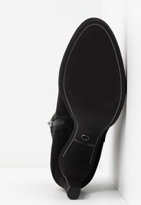 Mustat mokkanahkasaappaat nilkkapituisella pitkävetoketjulla, teräväkärkiset ja kumipohjaiset. Ominaisuuksiin kuuluu sileä pinta ja minimalistinen muotoilu.