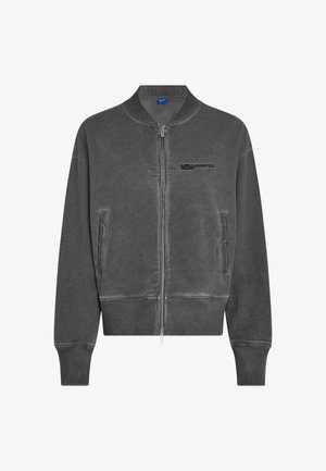 Pilkas bombonešis, pagamintas iš minkštos medžiagos, su užtrauktuko uždarymu, šoniniais kišenių, šonkauliniais rankogaliais ir išsiuvinėtu logotipu ant krūtinės.