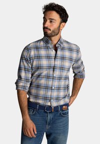 Blauw en beige geruite shirt met knoopsluiting en lange mouwen opgerold, voorzak, gouden logo borduring, gecombineerd met denim jeans en een blauwe riem.