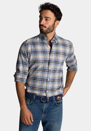 Blauw en beige geruite shirt met knoopsluiting en lange mouwen opgerold, voorzak, gouden logo borduring, gecombineerd met denim jeans en een blauwe riem.