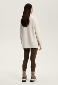 Maglione lavorato a maglia color beige chiaro con collo alto, maniche lunghe e orlo a coste; abbinato a leggings marroni e sneakers grigie.