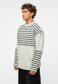 Lichtgrijze lange mouwen shirt met zwarte horizontale strepen, met een relaxte pasvorm en ronde halslijn, gecombineerd met donkere jeans.