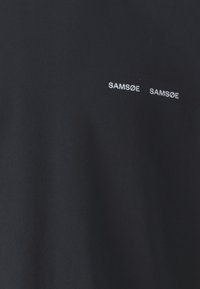 Tumedast puuvillast T-särk, millel on kaks valget "SAM[SØ] SAM[SØ]" logo. Materjal on sile ja klassikalise ümarat kaelust.