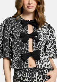 Top corto con stampa leopardata in bianco e nero, caratterizzato da maniche a sbuffo, tre decorazioni a forma di fiocco nero nella parte anteriore e un design con ritaglio centrale.