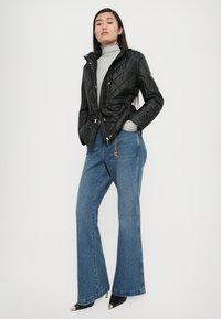 Black quilted jacket with a fitted waist and hood, paired with light blue wide-leg jeans and black pointed-toe heels with gold accents.