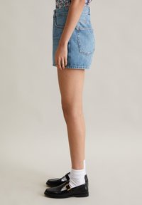Lichte blauwe denim shorts met hoge taille en een klassieke pasvorm, hebben een vijf-pocket ontwerp en een afgeronde zoom. Gepaard met zwarte instappers en witte sokken.