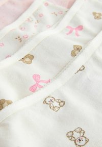 Vêtements pour bébé blancs avec des nœuds roses et de petits imprimés d'ours en peluche, avec un tissu doux et des bords festonnés.