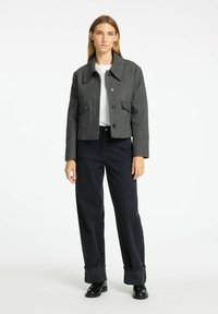 Giacca corta a spina di pesce grigia con ampio colletto, due tasche frontali e chiusura a bottone, abbinata a jeans larghi scuri e scarpe nere.