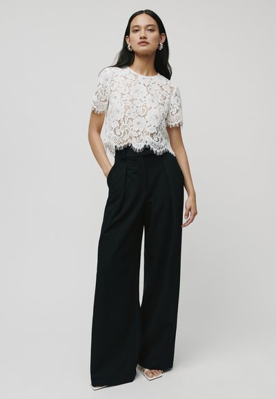 Witte kanten crop-top met korte mouwen en een scalloped zoom, gecombineerd met hoge zwarte vlinderbroek met een getailleerde pasvorm.