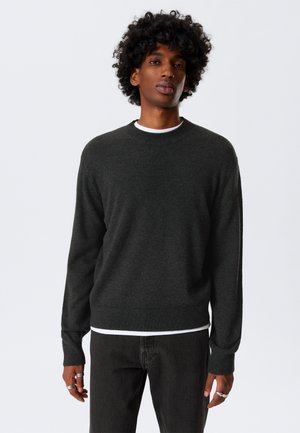 Dark gray knit sweater with a round neck, ribbed cuffs, and hem. Worn over a white T-shirt, featuring a smooth texture and simple design.