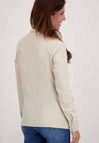 Licht beige overhemd met lange mouwen en een gladde textuur, met knoop manchetten en een klassieke kraag, gecombineerd met blauwe denim jeans.