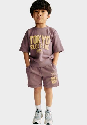 Lila bomulls sweatshirt med kort ärm och matchande shorts med "TOKYO SKATE PARK" i guldtext, kombinerat med vita och turkosa träningsskor.