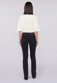 Černé zvonové džíny s hladkým povrchem a dvěma zadními kapsami; spárované s volným bílým topem. Žádné viditelné kovové prvky ani vzory.