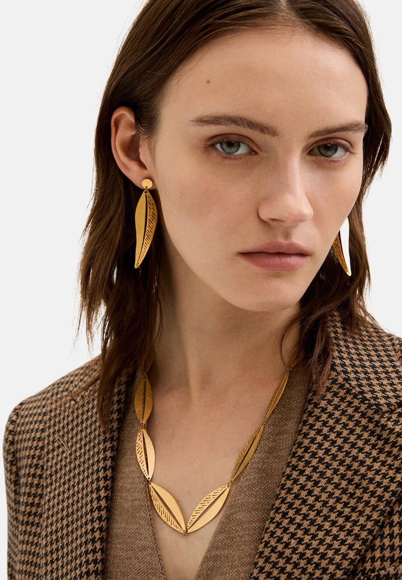 Guldtonet smykker med aflange bladformede designs med ætsede detaljer, parret med en ternet brun blazer og en taupe sweater.