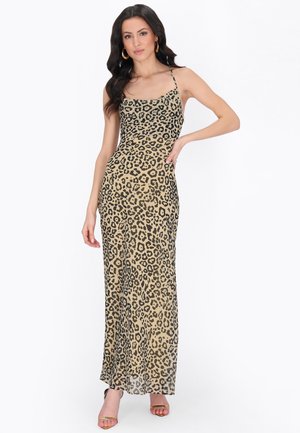 Kvinde iført en beige leopardprint, ærmeløs maxikjole med tynde stropper, stående med den ene hånd på hoften og iført guldringeøreringe.