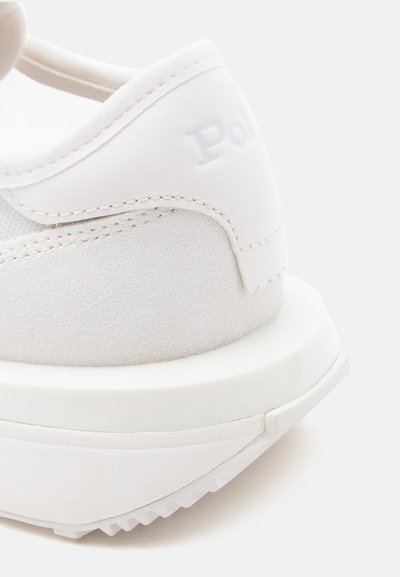 Κοντινή λήψη της φτέρνας ενός λευκού αθλητικού παπουτσιού με υλικά από σουέτ και δέρμα, παχύ πέλμα και μερικώς ορατό ανάγλυφο όνομα της μάρκας «Polo».