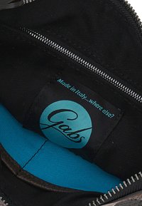Interno in tessuto nero di una borsa con una fodera turchese e un'etichetta con il logo Gabs. Presenta una cerniera metallica per la chiusura.