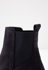 Námořnické semišové kotníkové boty s elastickým textilním panelem, elegantním tvarem a poutkem pro snadné obouvání. Hladký povrch s jemným prošíváním.
