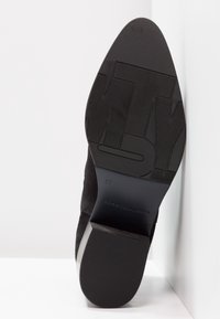 Suola di scarpa in suede nera con gomma testurizzata e finitura liscia. Presenta marchi del logo in rilievo e indicazione della taglia sul tallone.