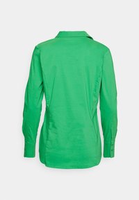 Chemise verte à manches longues avec col, vue de dos, avec poignets boutonnés et coupe légèrement cintrée.