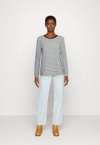 Camisola de manga longa riscada em azul-marinho e branco, combinada com jeans de perna reta em azul-claro e botas de plataforma em tom de caramelo. Tecido suave e ajuste descontraído.