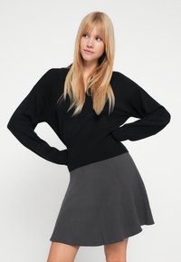 Pulover negru tricotat cu mâneci largi, asortat cu o fustă plisată gri. Texturi moi, croială lejeră și culori contrastante care îmbunătățesc aspectul.