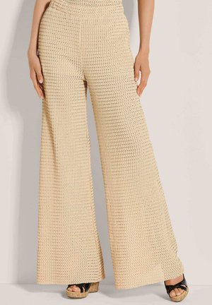 Beige wijde broek met een textuur gebreid patroon, gedragen met zwarte plateau sandalen op een lichte achtergrond.