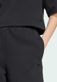 Sudadera de algodón negra con mangas cortas, con un diseño recortado y un pequeño logo negro en la parte inferior. Combinada con joggers a juego.