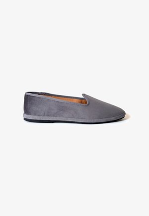 Scarpa piatta grigia slip-on con una morbida texture in camoscio e punta arrotondata, mostrata di profilo su sfondo bianco.
