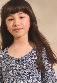 Vestito floreale in blu navy, con motivi di fiori rosa e bianchi, scollo a barca e piccoli bottoni neri. Tessuto morbido con maniche corte a sbuffo.