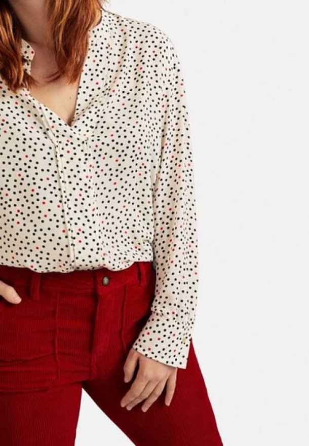 Blouse blanche à pois noirs et rouges, col en V, associée à un pantalon en velours côtelé rouge taille haute avec des panneaux texturés.