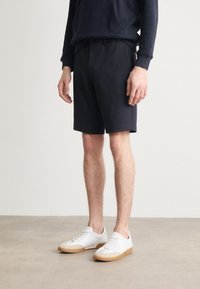 Menns sorte shorts laget av et mykt stoff med elastisk midje, kombinert med hvite sneakers med gummisåle og snøring.