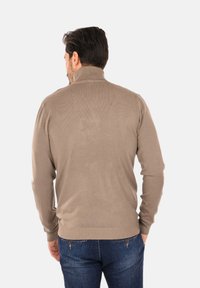 Maglione lavorato a maglia beige con collo alto, polsini e orlo a coste. Texture liscia, design aderente e dettagli sottili sui bordi del collo.