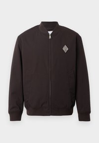 Must must jacket, mille ümmarguse kaelusega, tõmbluku sulgemisega, kahe küljetaskuga ja vasakul rinnal rombikujulise logoga plaastriga.