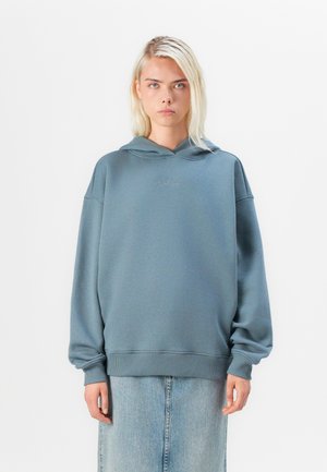 Light blue oversized hoodie in soft fabric with a drawstring hood, ribbed cuffs, and a small logo embroidered on the chest. Pair with denim.