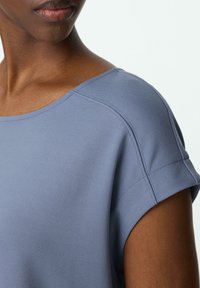 Grau-blaues kurzärmliges Oberteil mit weitem Ausschnitt, aus weichem Stoff und sichtbaren Nahtdetails an den Schultern und Ärmeln.