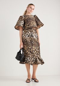 Leopardmønsterkjole i gull og brun, med korte pufferm, en volangkant og kombinert med en liten svart håndveske og sandaler.