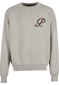 Suéter gris con un cuello redondo acanalado, mangas largas y una pequeña letra "P" de color marrón oscuro bordada en el pecho. Textura suave.
