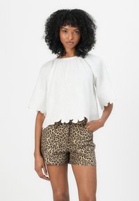 Blouse blanche brodée avec un motif floral et un ourlet scallopé, associée à un short imprimé léopard dans des nuances de marron et de beige.