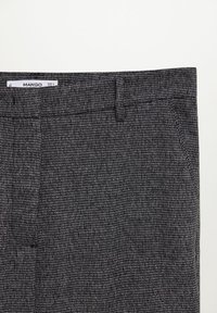 Gros plan d'un pantalon texturé gris foncé avec passants de ceinture et une étiquette de marque Mango visible à la taille.