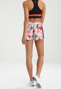 Urheilulliset kukkashortsit, joissa on vaaleanpunaisia ja punaisia ruusuja, elastinen vyötärö ja sivuilla mustat yksityiskohdat, yhdistettynä mustaan urheiluliiviin ja valkoisiin tennareihin.